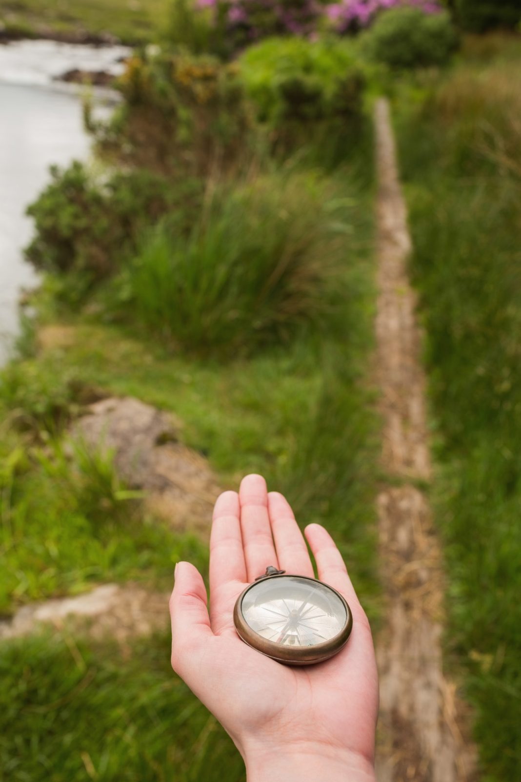 Hand holding old fashioned compass showing the way on a country trail Hand holding old fashioned compass showing the way on a country trail